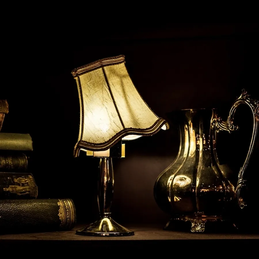 Brass table lamp with a glowing pleated shade beside old books