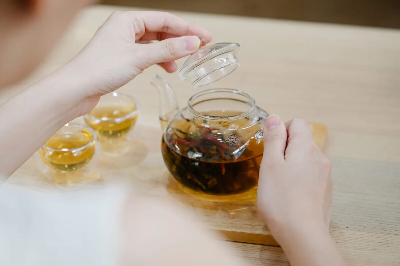 Hands lifting the lid of a glass teapot